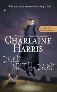 Book cover for "Dead Until Dark" by Charlaine Harris, featuring a figure in a black cloak floating against a dark sky with a small house burning below.